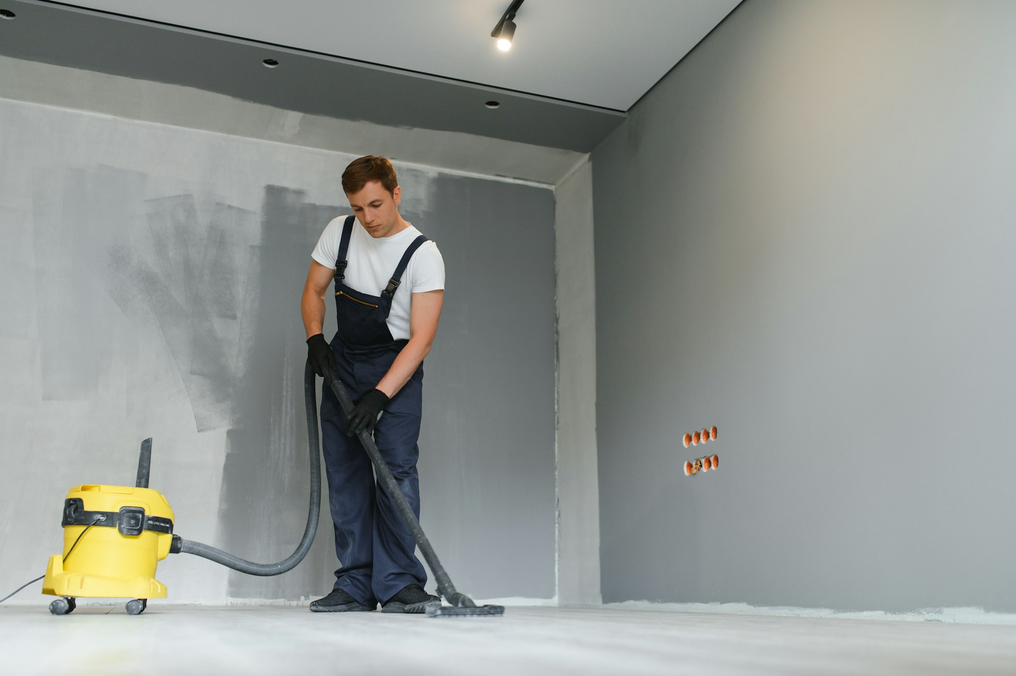 A worker using a vacuum cleaner removes construction debris.