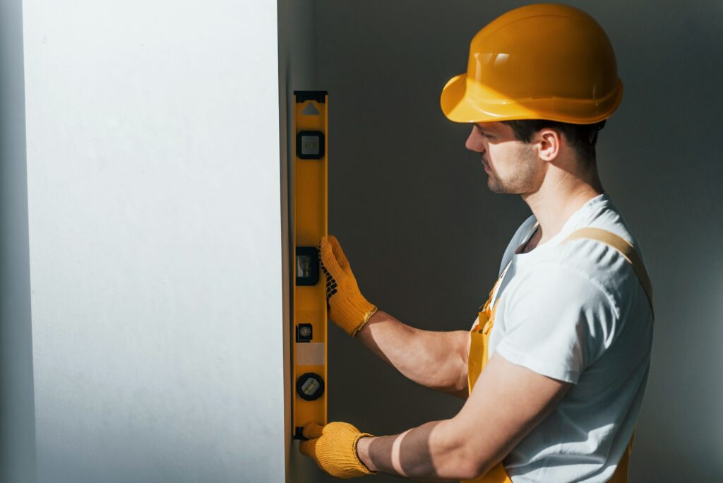 Handyman in yellow uniform checks levels of wall. House renovation conception