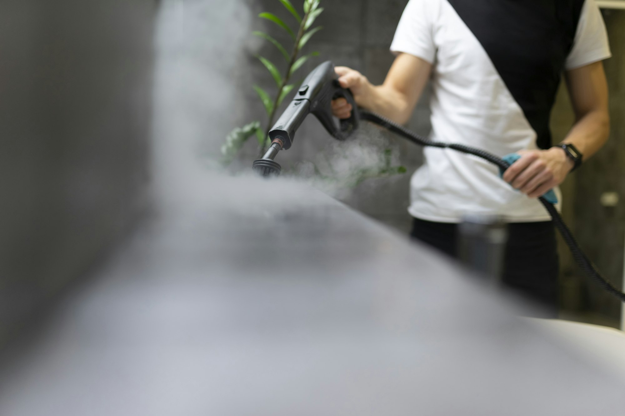 Worker of a cleaning company is cleaning the tiles in the bathroom with steam